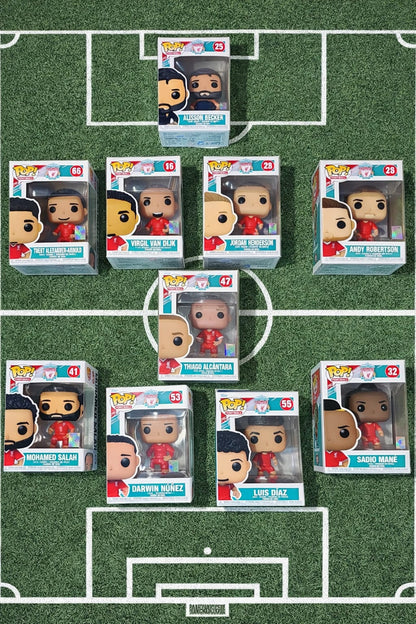 Liverpool FC Funko Pop collection featuring Mohamed Salah, Jordan Henderson, Darwin Núñez, Luis Díaz, Sadio Mané, Thiago Alcântara, Trent Alexander-Arnold, Virgil van Dijk, Andy Robertson, and Alisson Becker arranged in a football formation on a grass pitch with field markings.