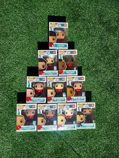 Ten Liverpool FC Funko Pop figures of Mohamed Salah, Jordan Henderson, Darwin Núñez, Luis Díaz, Sadio Mané, Thiago Alcântara, Trent Alexander-Arnold, Virgil van Dijk, Andy Robertson, and Alisson Becker displayed in a pyramid formation on a grass-textured background.